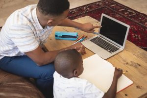 high-angle-view-african-american-father-helping-his-son-with-homework-laptop-table_13339-347873