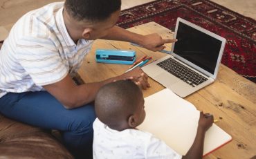high-angle-view-african-american-father-helping-his-son-with-homework-laptop-table_13339-347873